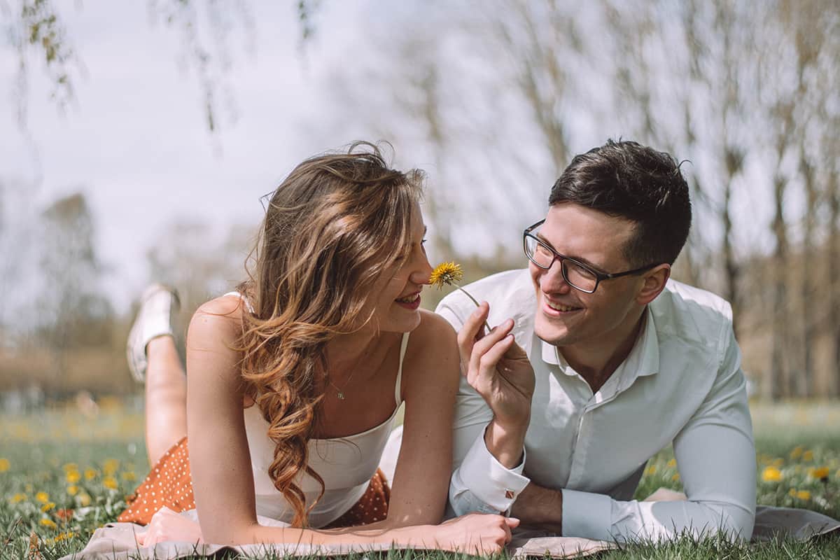man and woman smelling flowers and smiling outdoors
